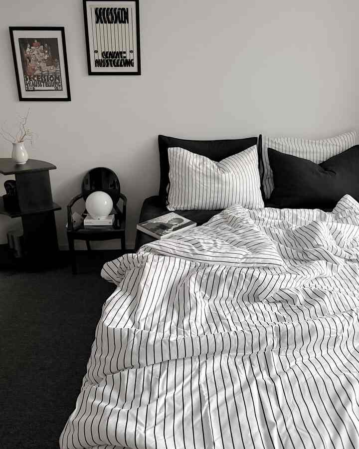 Monotone black and white bedroom featuring striped bedding and a small armchair, creating a simple and modern atmosphere