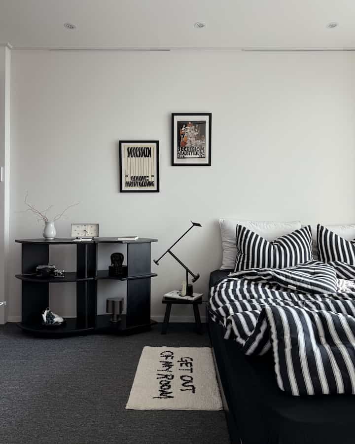 Monotone black and white bedroom featuring striped bedding, black shelf, and bedside table in a simple modern style