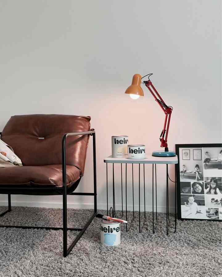 白い壁とグレーのラグのある空間に、茶色のレザーアームチェアと赤いフロアランプが配置された温かみのあるインテリア