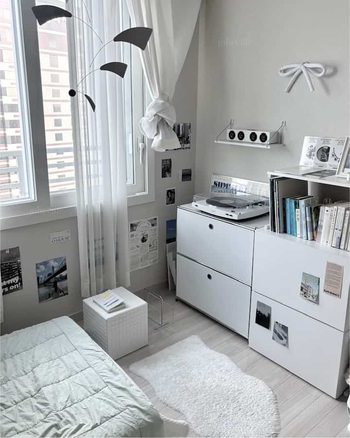 白とモノトーンの調和がとれた寝室、白い収納家具とカーテン、居心地の良いラグが配置された印象的なインテリア