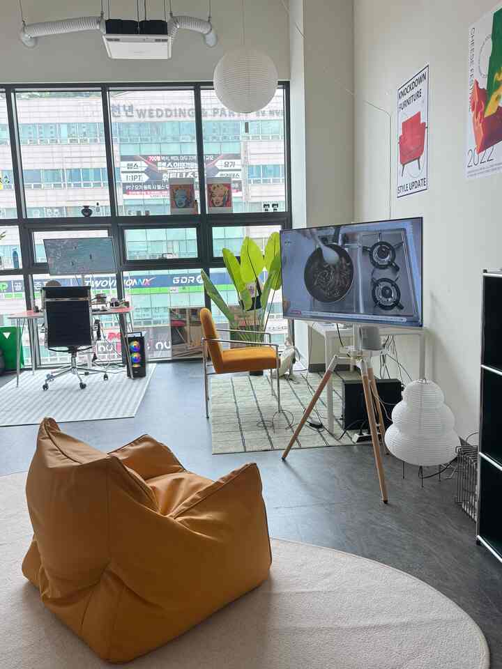 白と茶色のトーンのホームオフィス兼リビング、ビーンバッグソファとミッドセンチュリーモダンのアームチェアが配置された居心地の良い空間