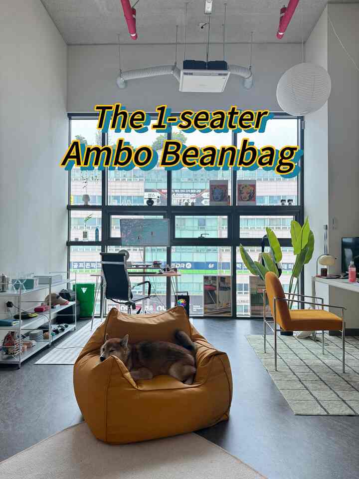 明るい黄色のビーズクッションソファが中央に配置され、大きな窓際にあるモダンなホームオフィスの机と犬がいる明るく現代的なリビングスペース