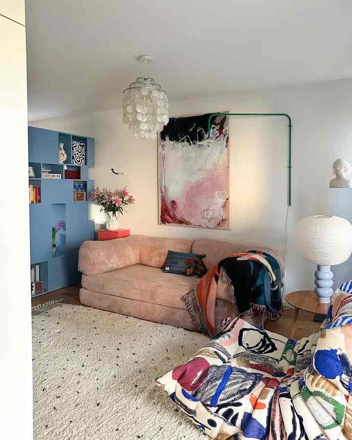 Bright living room with pink sofa and blue cabinet, featuring large abstract painting and pendant light, creating a stylish atmosphere
