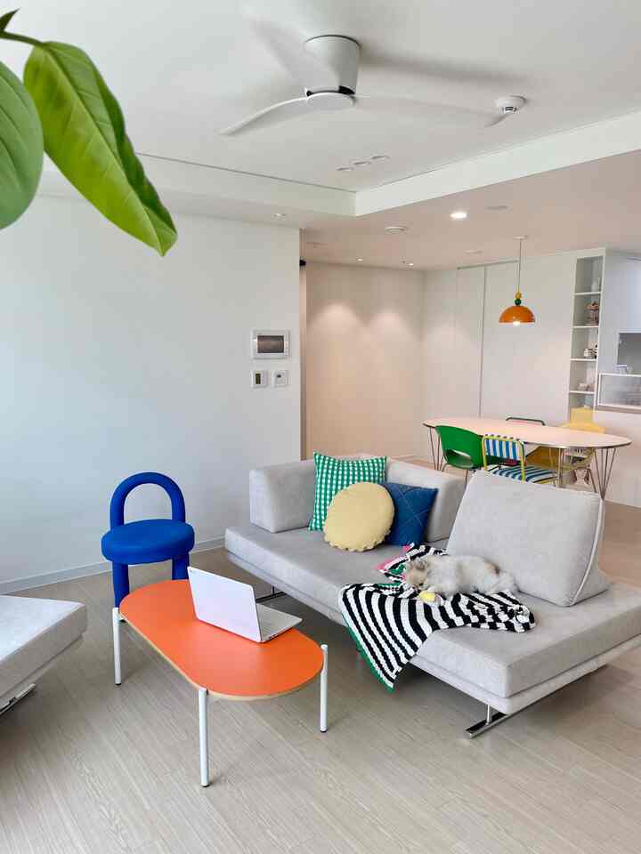 白を基調としたモダンなリビング、オレンジのコーヒーテーブルと青い椅子が配置された印象的な空間