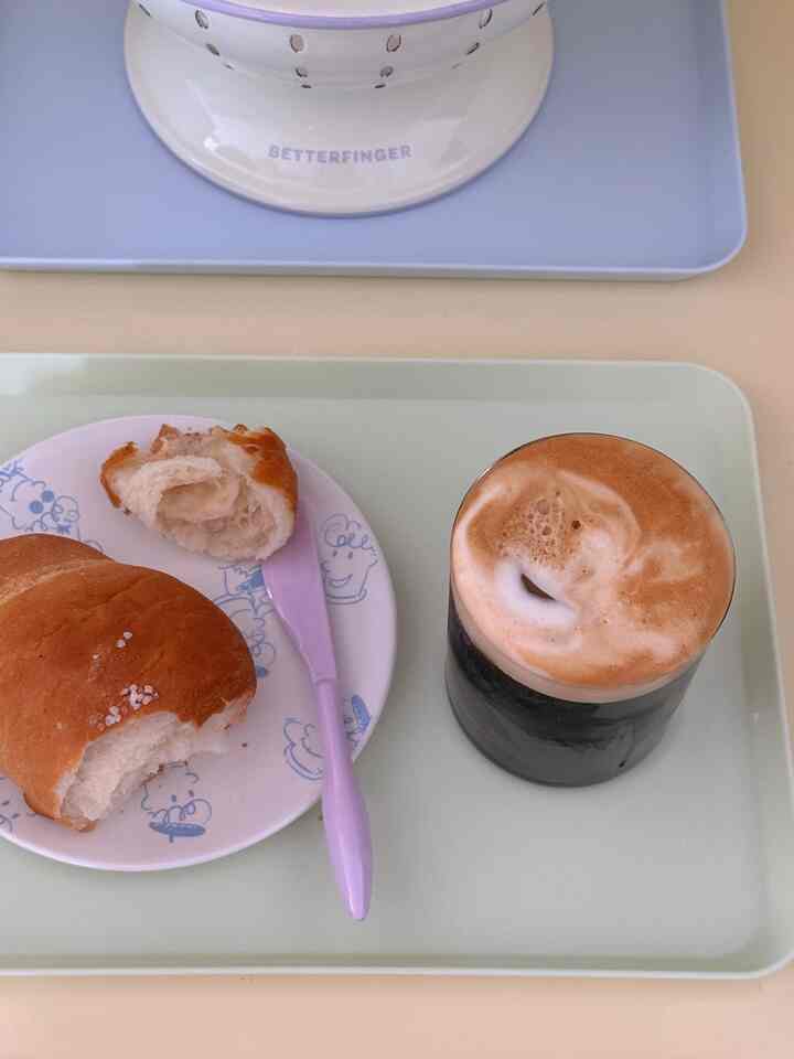 ミント色のトレイの上にブラウンのパンとラベンダー色のナイフ、クリームが乗ったコーヒーが置かれた居心地の良いおうちカフェ風のキッチンの写真