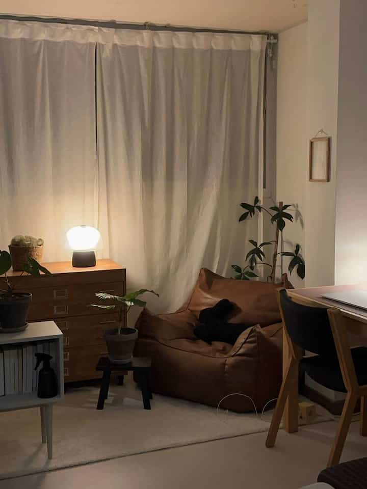 木目調とブラウンが調和する寝室、ビーンバッグソファと植物、テーブルランプが配置された雰囲気のある小さな部屋