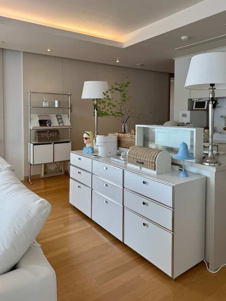 Bright white and wood-tone living room featuring a cabinet and floor lamps, creating a cozy and natural interior space