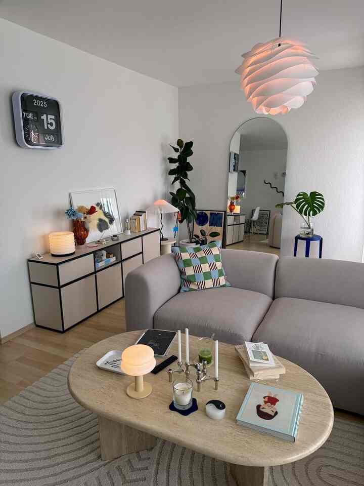 Modern living room with gray sofa and brown wood-tone table, featuring an arched mirror and plants in a calm space
