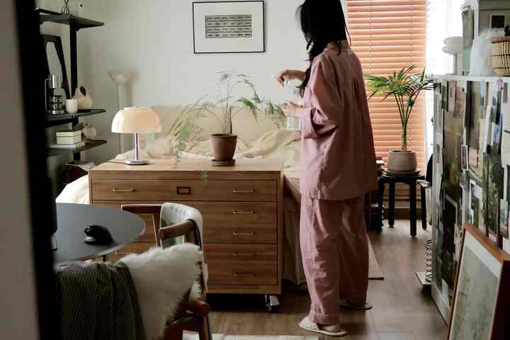 木目調とベージュの調和が取れた8畳ワンルーム寝室、ベッドとチェスト、植物が配置された雰囲気のあるナチュラルモダンな空間