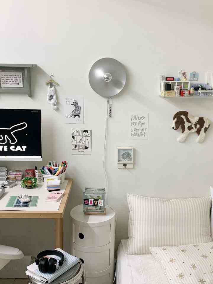 白を基調とした寝室兼ホームオフィス、机やナイトテーブル、シルバーの壁掛けライトが配置された清潔感のある空間