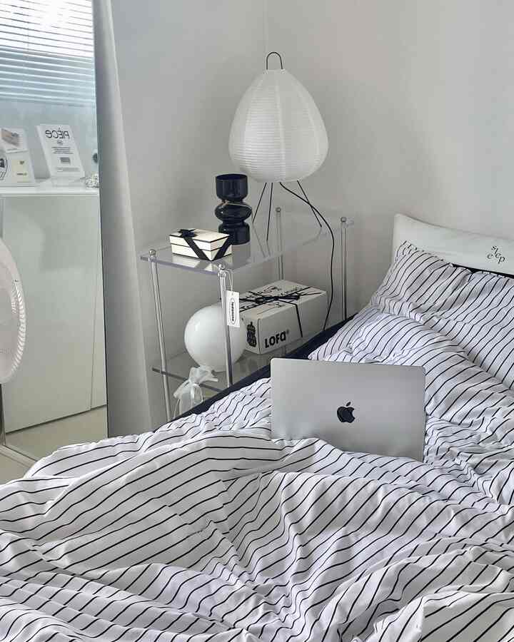 White-toned bedroom featuring striped bedding and transparent acrylic shelf with a modern and clean aesthetic