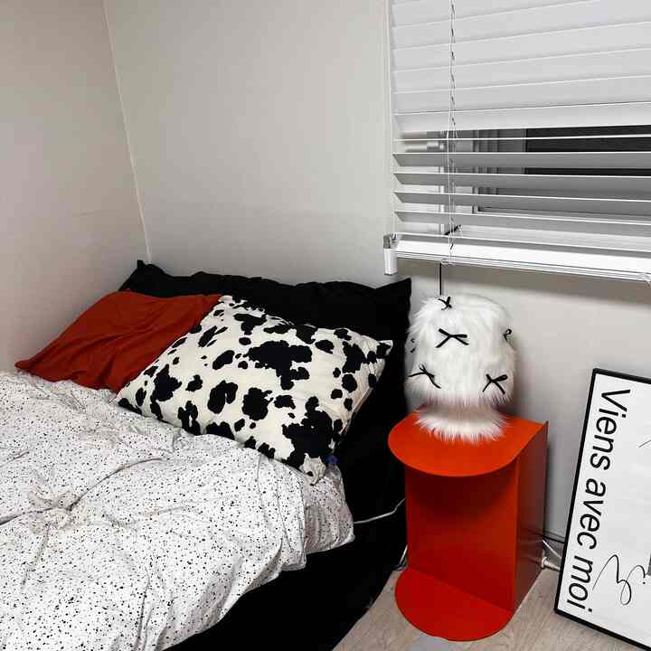 A modern and simple studio bedroom featuring a black and white bedding set with orange accent side table and cozy cushions