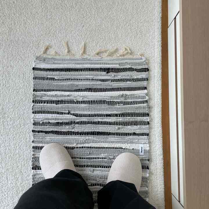 ホワイトの床と木製のドア横に置かれたストライプのバスマットとスリッパのある空間