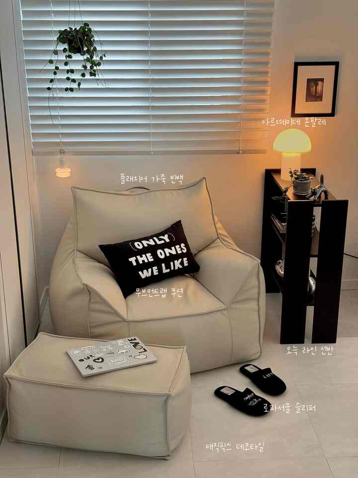 温かみのあるベージュとホワイトのトーンの居心地の良いリビングコーナー、ビーズクッションソファと棚、落ち着いた照明が配置された空間