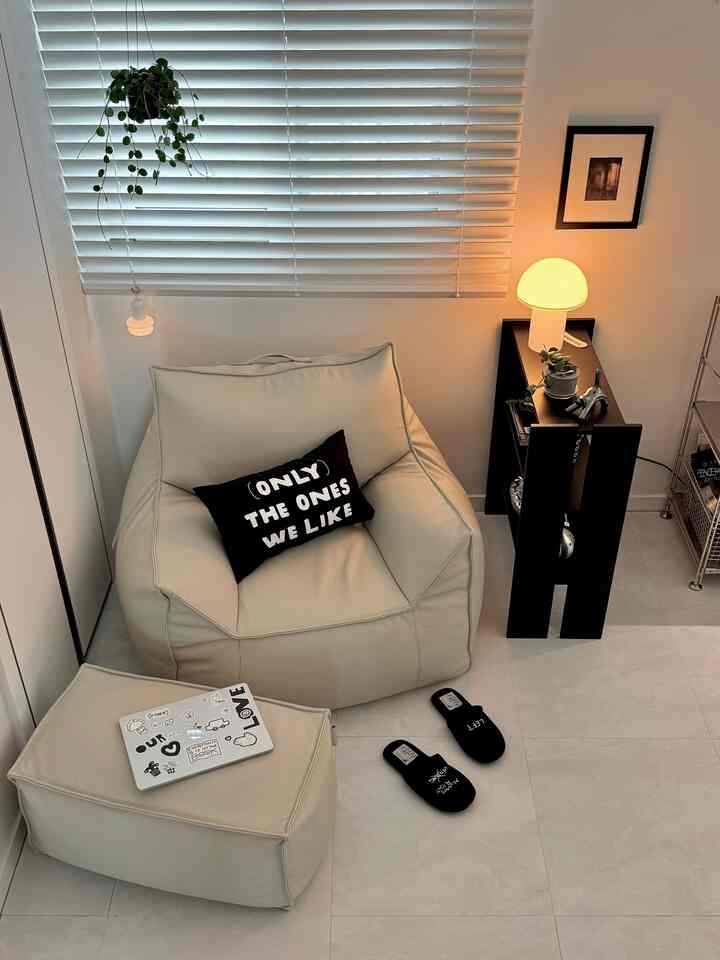 ベージュの温かみある色調の寝室、ビーズクッションソファとオットマン、フロアランプが配置された雰囲気のあるインテリア