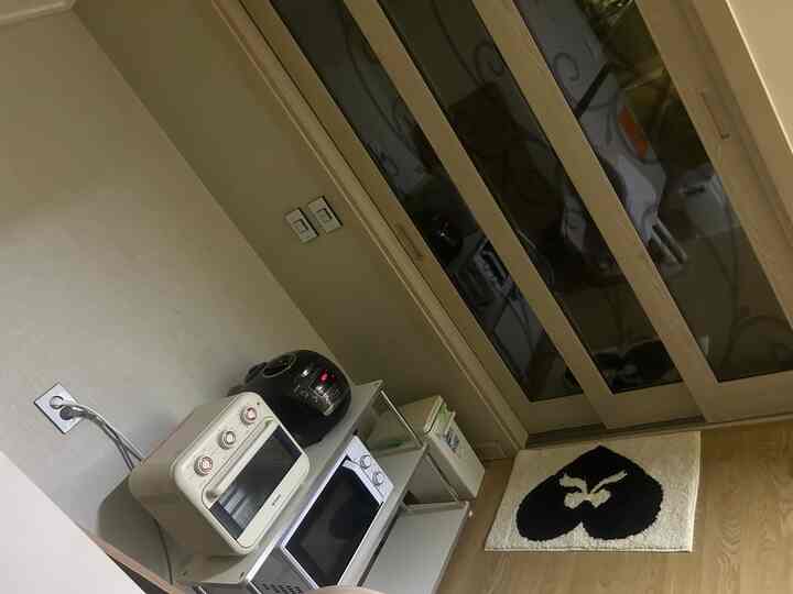 白とダークブラウンの色調のキッチン、オーブンや炊飯器、電子レンジが整理されたコンパクトな空間とリボンハート柄のバスマット