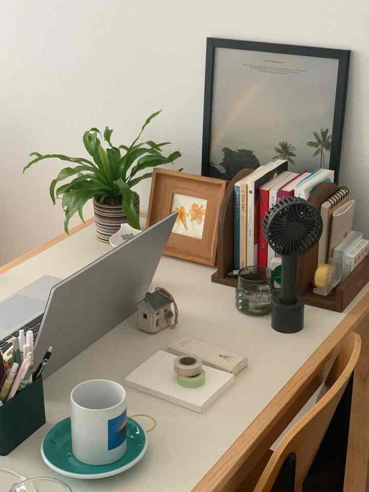 白と木目調の小さなホームオフィスのデスク空間、本と植物が配置された落ち着いた作業環境