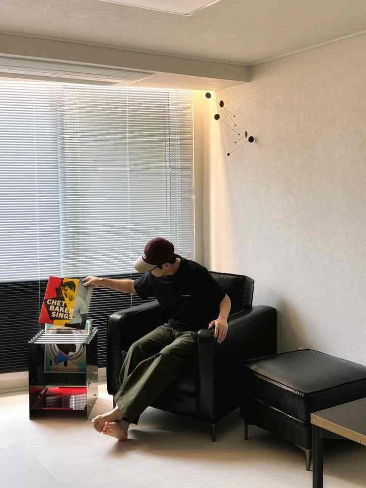 Bright and clean study with black leather armchair and stool, magazine rack and vinyl albums by window create cozy atmosphere