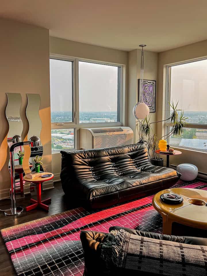 Modern living room corner with black leather sofa, red rug, wood flooring illuminated by warm golden hour light