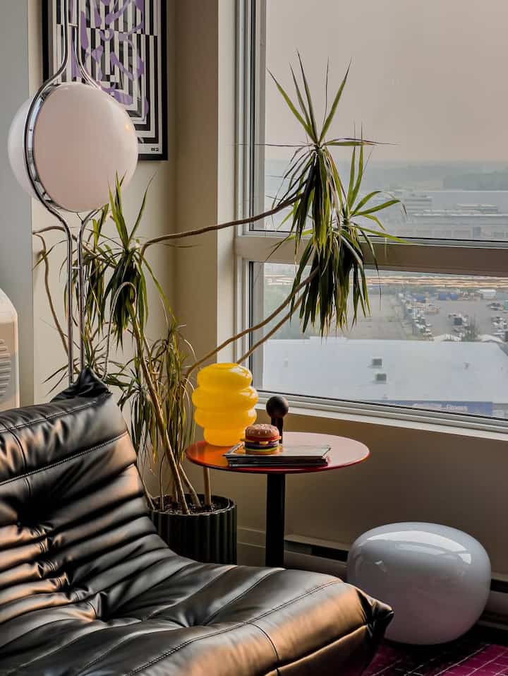 Natural-toned modern living room featuring a black leather sofa, red side table, and yellow vase harmoniously arranged