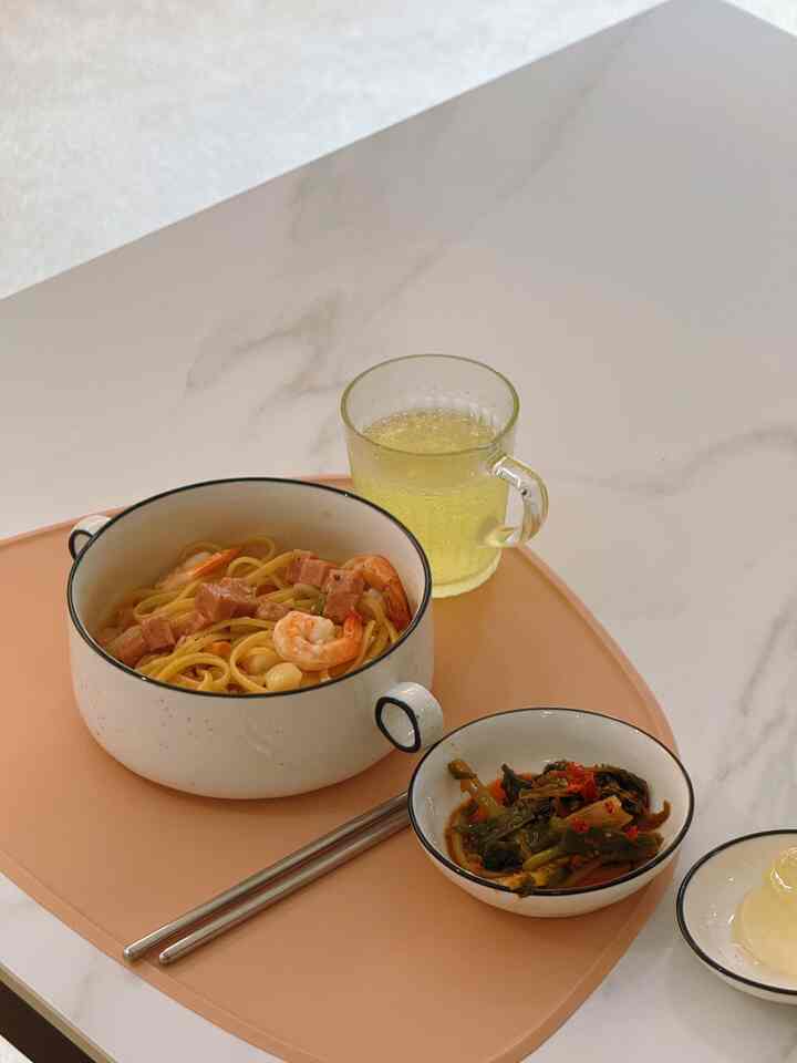 柔らかなベージュトーンのダイニングテーブルに、エビとハム入りの麺、惣菜の小鉢、飲み物が置かれたすっきりとしたテーブルセッティング