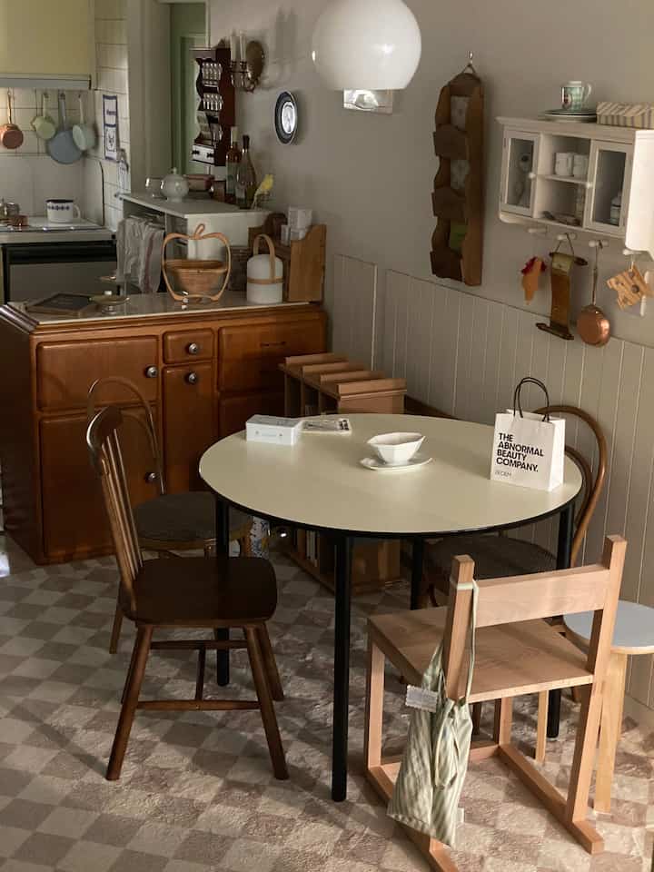 ナチュラルな色調とヴィンテージ家具が配置されたアパートのキッチン、丸いダイニングテーブルと木製チェアが印象的な温かみのある空間