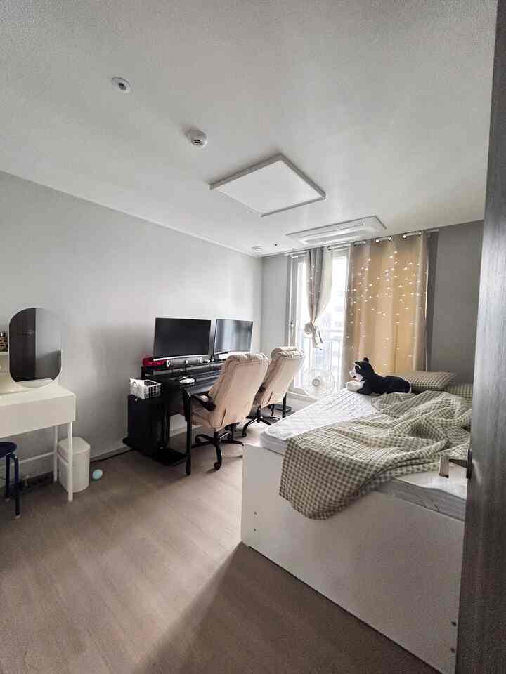 白とベージュのトーンの寝室兼ホームオフィス、二つのコンピューターデスクと椅子が配置された機能的な空間