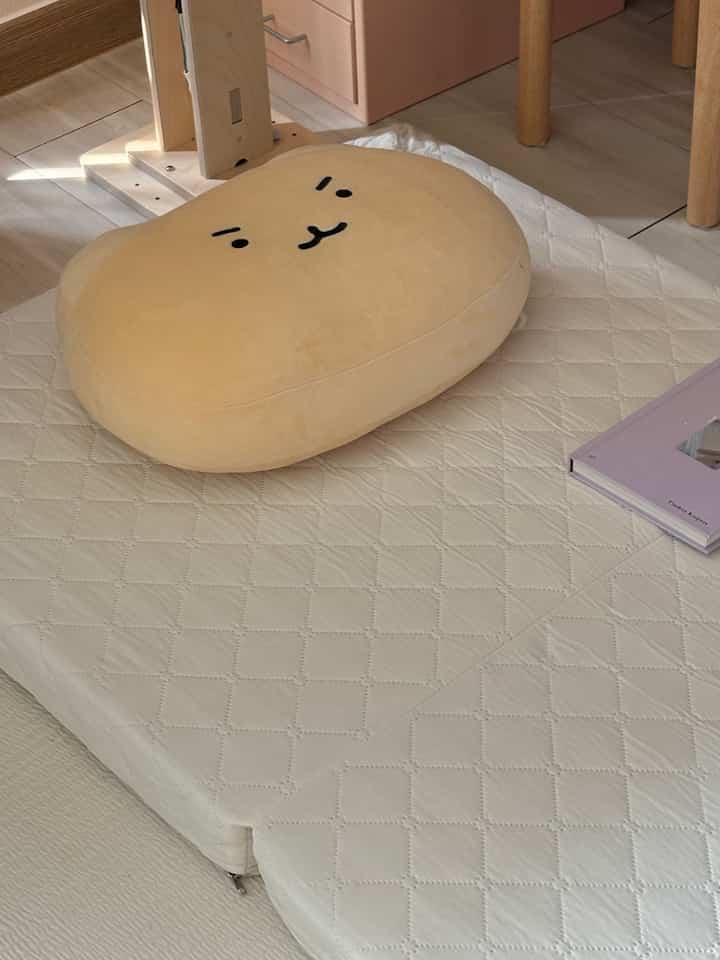 柔らかなベージュとホワイト調の子供部屋、かわいいキャラクター枕とピンクの化粧台が温かみのある雰囲気を作る部屋