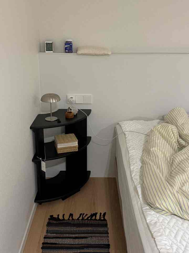 白と木目調の寝室、コーナーナイトテーブルと金属製テーブルランプ、ストライプの掛け布団カバーが配置された雰囲気のある空間