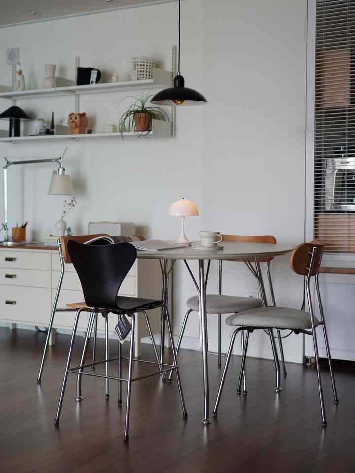 白と木目調が調和する小さなダイニング空間、丸いテーブルと多様な椅子が配され、シンプルでミニマルな雰囲気のインテリア