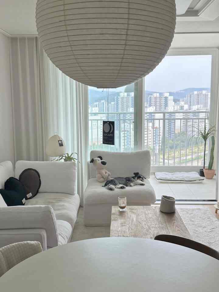 白と木目調が調和したリビング、モジュラーソファとアカリ照明が配置された落ち着いた空間