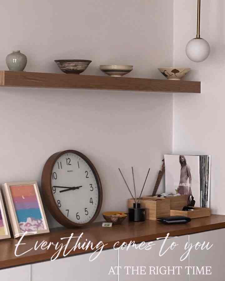 ホワイトの壁とブラウンの木製棚、時計が配置されたナチュラルな印象のキッチン空間