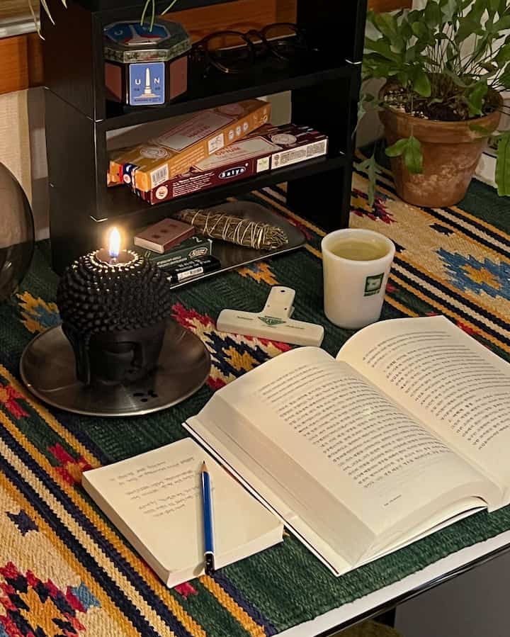 レトロな雰囲気のデスク、ヴィンテージの植物、香りのアイテム、灯されたキャンドルと本が配置された温かみのある空間