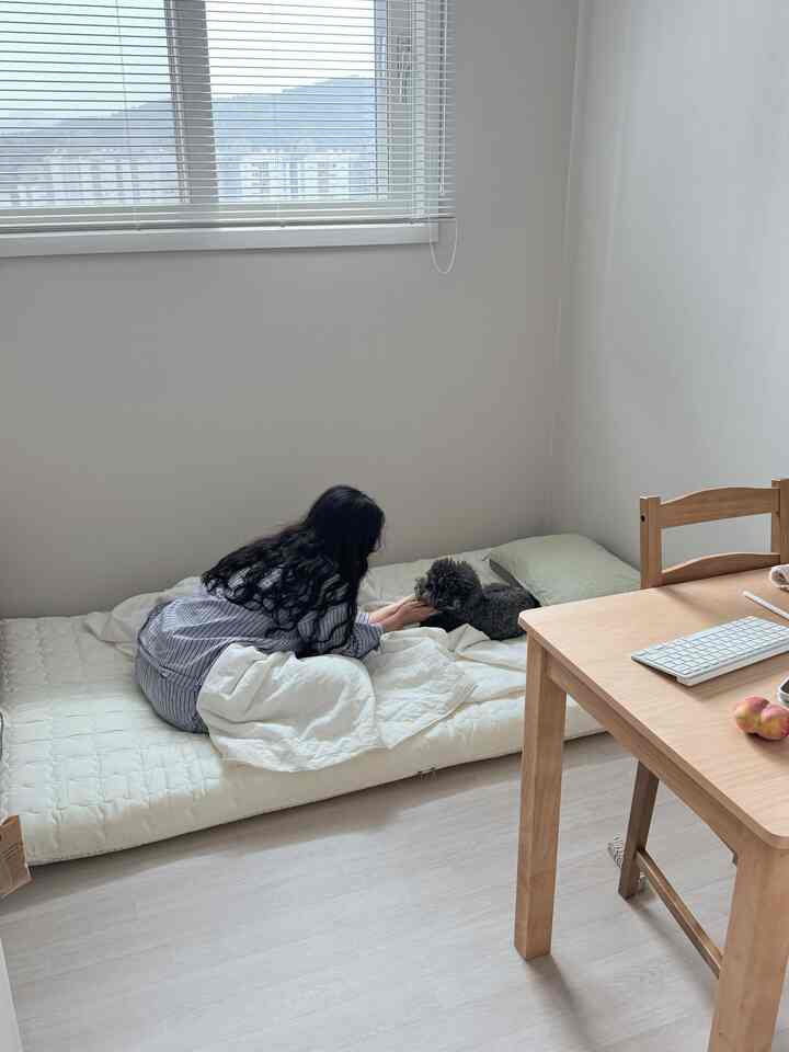 ベージュと木目調の小さな寝室、マットレスの上で犬と触れ合う温かみのある空間