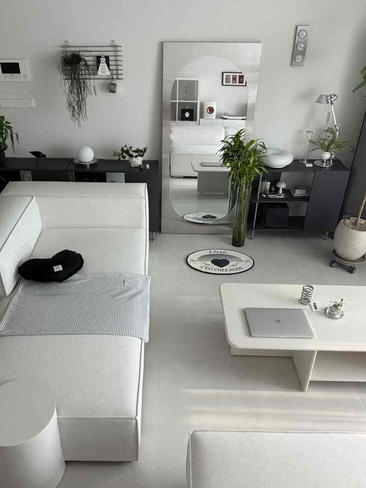 ホワイトとナチュラルカラーが調和するリビング、ホワイトのソファとコーヒーテーブル、大きな鏡と植物が配置されたシンプルモダンなインテリア