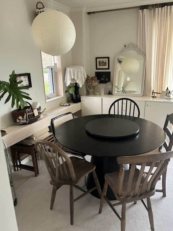 ナチュラルな色調のダイニングルーム、中央に黒い丸テーブルと異なる木製の椅子が配置された温かみのある空間