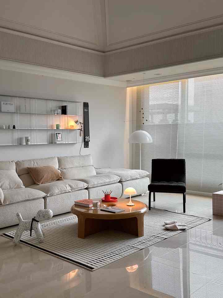 アイボリー調のモダンでシンプルなリビング、クリーム色のソファと丸いコーヒーテーブル、黒い椅子が配置された落ち着いた空間