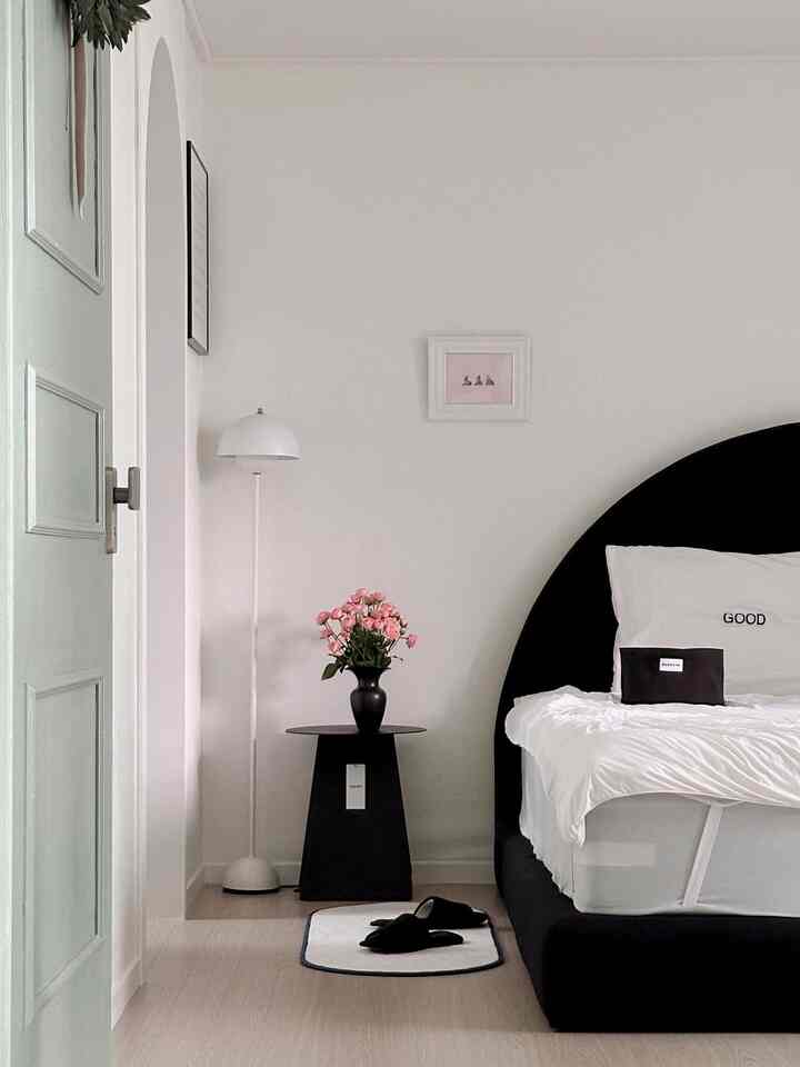 Monotone bedroom featuring a black bed, nightstand, and floor lamp in a simple setting