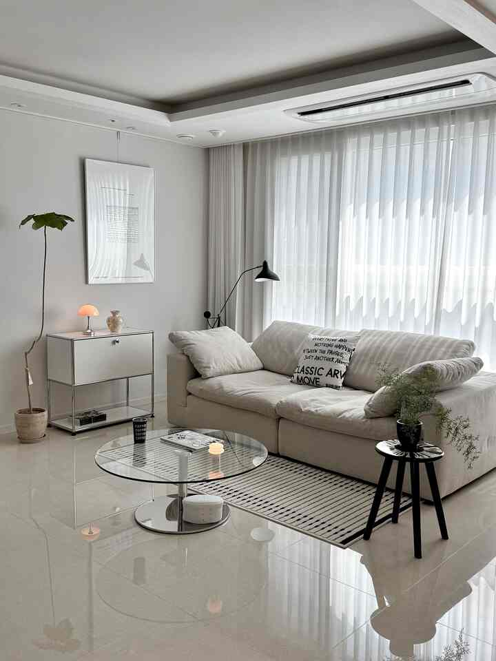 白とシルバーのトーンのリビング、ベージュのソファとストライプのラグ、植物とシンプルな照明が配置されたモダンな空間