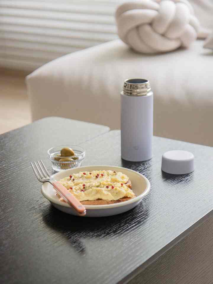 ウッドトーンとベージュの色調が特徴のリビング、サイドテーブルに簡単なブランチセットが置かれた落ち着いた空間