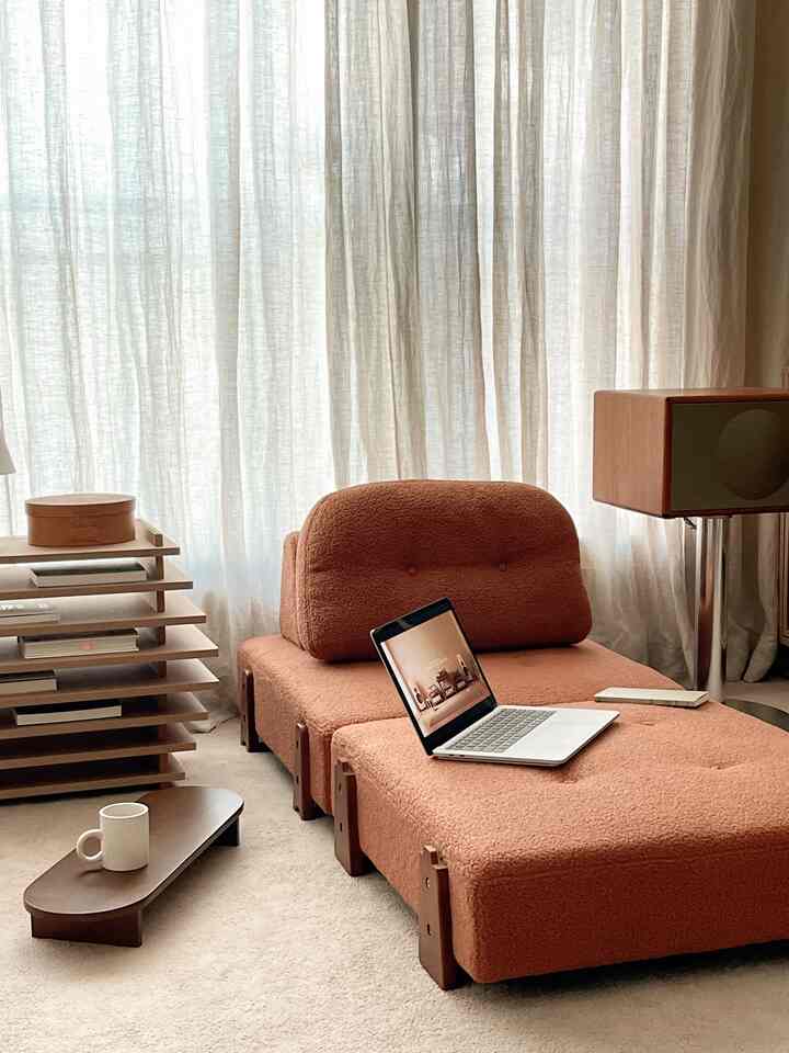 Cozy small living space in warm beige tones with rust-brown fabric sofa bed and wood-tone furniture