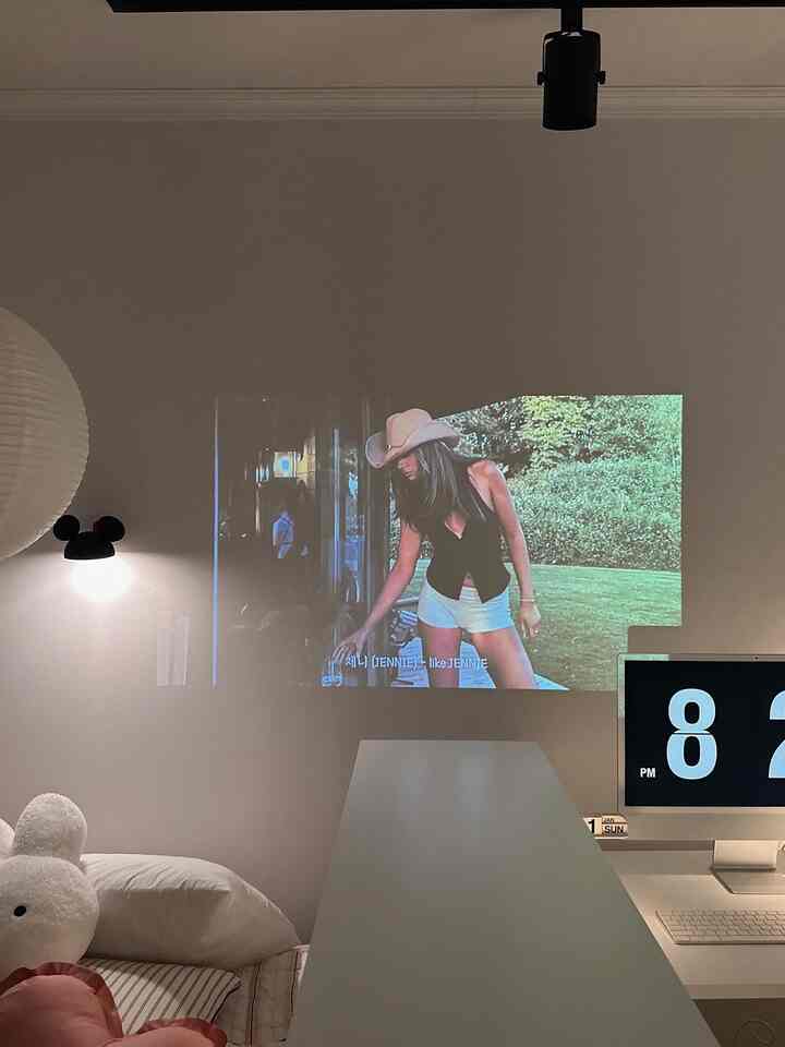 白を基調としたワンルーム、ベッドとモニタースタンドが配置されたシンプルで居心地の良いホームシネマ空間