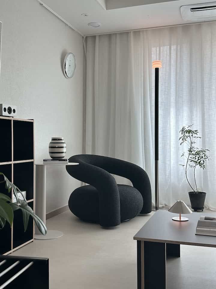 Gray and white toned living room featuring black armchair, side table, floor lamp, and plant in a simple modern space