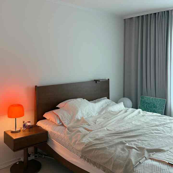 シンプルな白と茶色のトーンの寝室、木製ベッドフレームと暖色のムードライト、グレーのカーテンが配置された雰囲気のあるインテリア