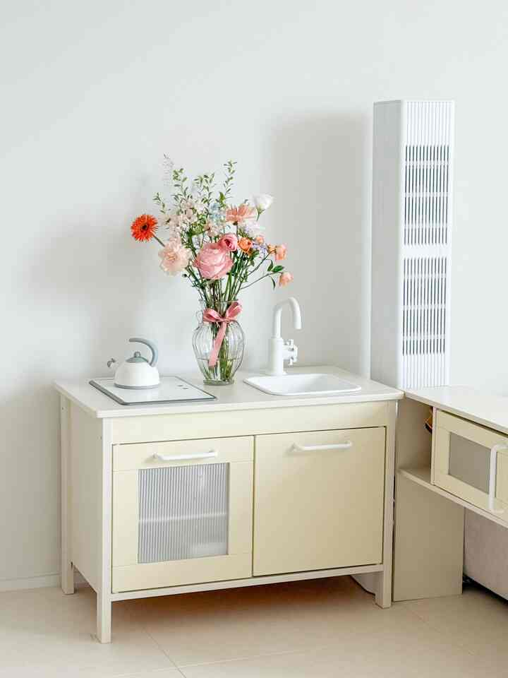 White and beige toned kitchen play area featuring a vase of flowers and a kettle centrally placed, creating a neat and charming kids' room decoration