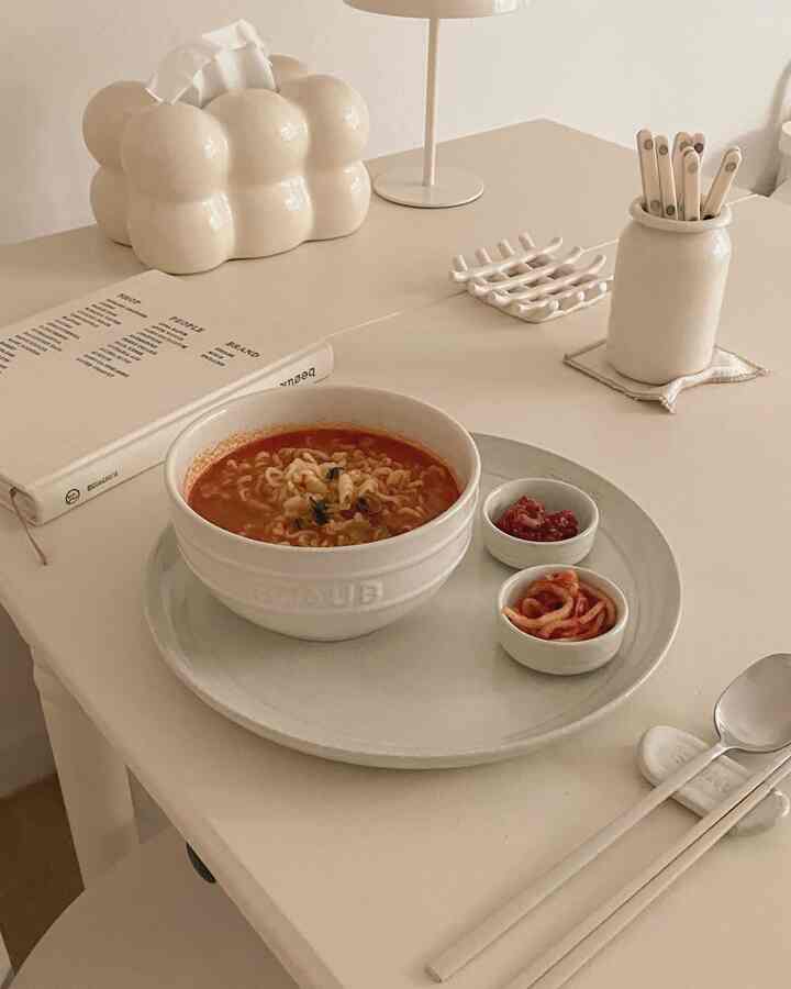 ベージュと白のトーンのダイニングテーブルにラーメンと小皿が配置された、ミニマルなおうちカフェの雰囲気のあるインテリア