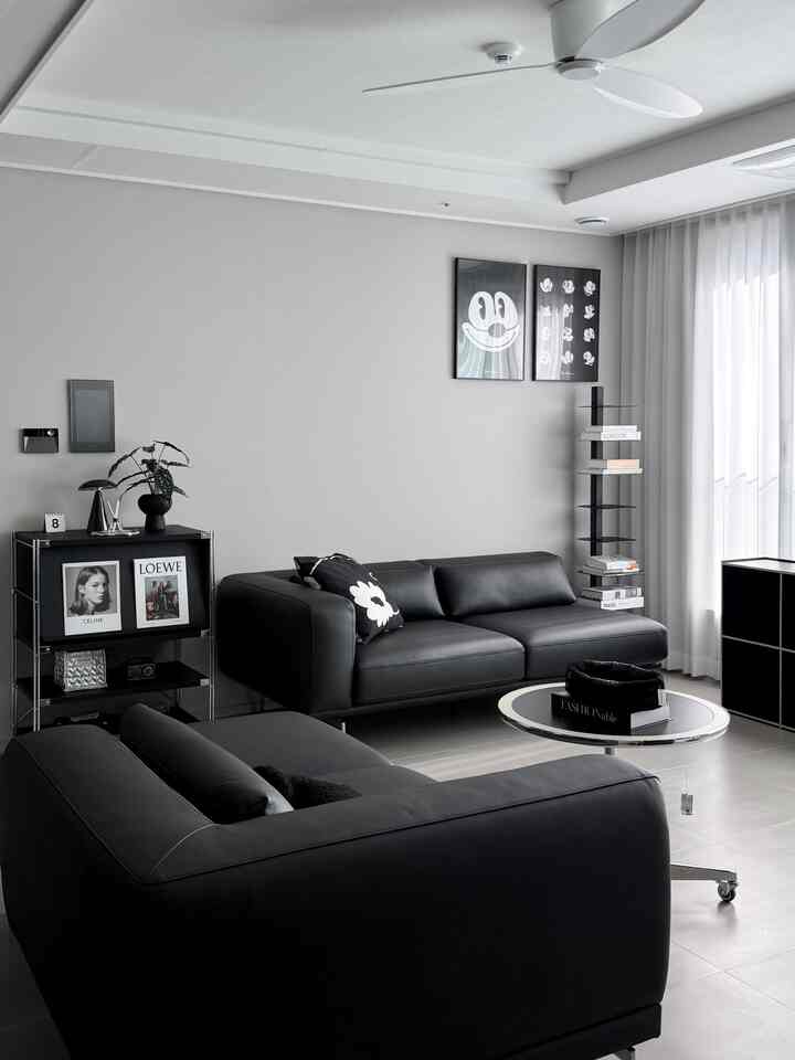 モノトーンの黒と白のリビング、2つのレザーソファと丸テーブル、壁の棚、大きな窓のカーテンが配置されたモダンなインテリア