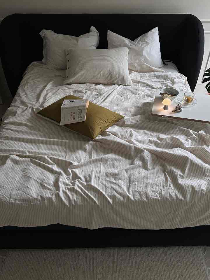 白とベージュの色調の寝室、黒のベッドフレームと枕、ナイトテーブルが配置された落ち着いた雰囲気のインテリア