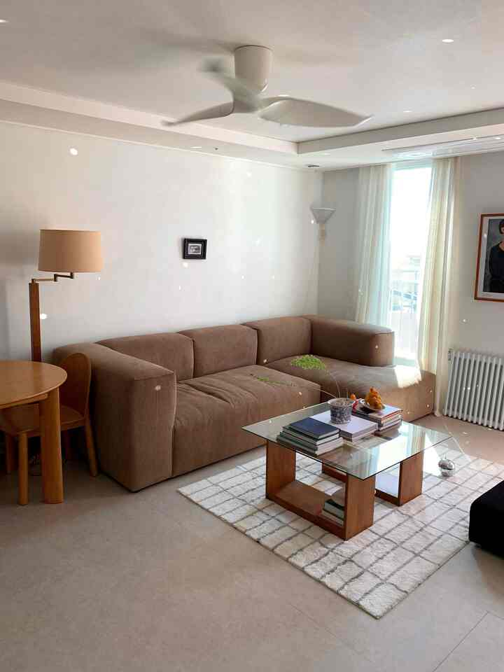 明るいホワイトとブラウンの色調のリビング、広いブラウンのソファとガラストップのコーヒーテーブルが配置された雰囲気のあるインテリア