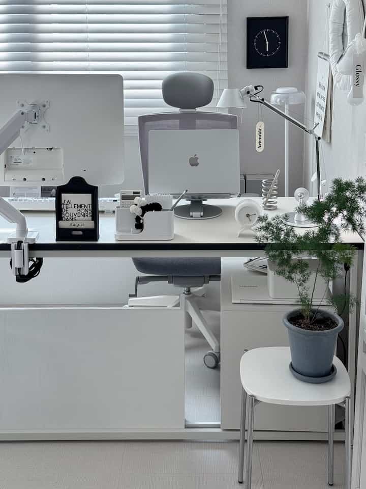 White and gray toned study-style home office featuring a clean desk with monitors, office chair, desk lamp, and plant in a modern interior